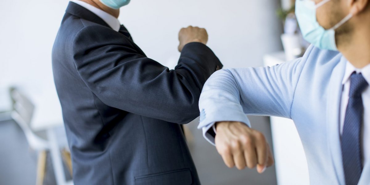 Two colleagues avoid a handshake when meeting in the office and greet with elbows bumping